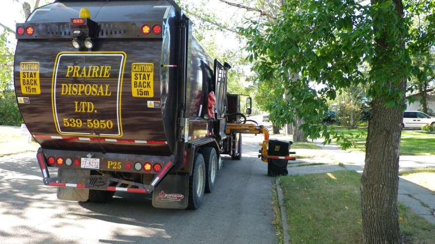 Brown Prairie Disposal truck with the arm out picking up a residential waste bin