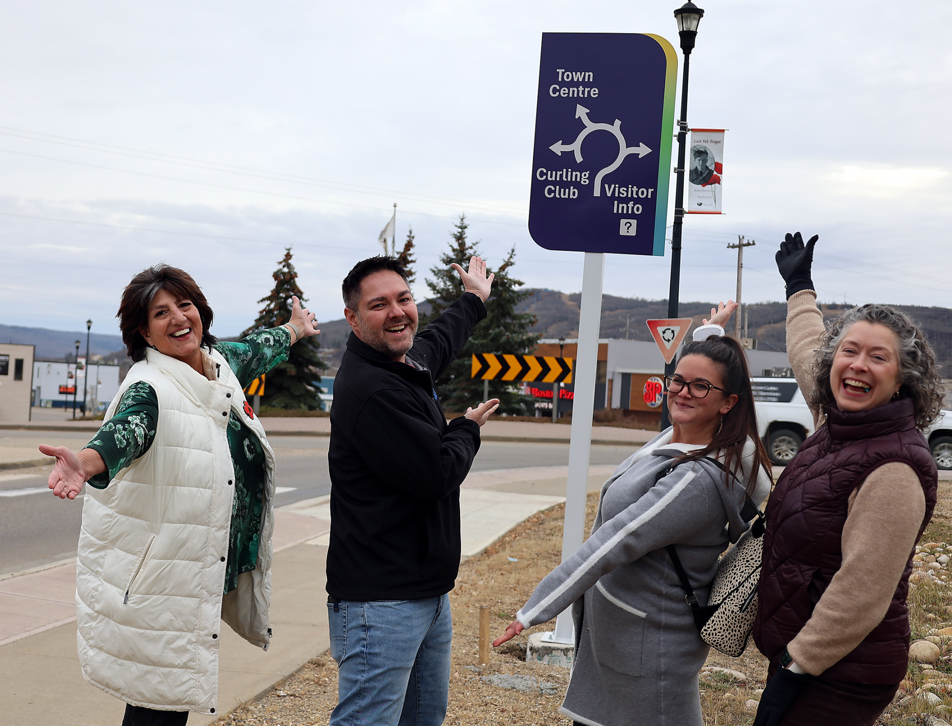 Council poses with a wayfinding sign directing people to the Town Centre, the Curling Club, and the Visitor Information Centre